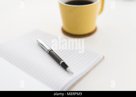 Close-up del libro e la penna dalla tazza di caffè su sfondo bianco Foto Stock