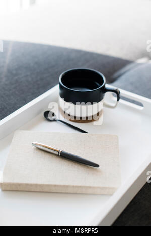 Close-up di penna sul diario dalla tazza di caffè nel vassoio Foto Stock