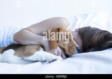 Donna sdraiata con beagle su letto di casa Foto Stock