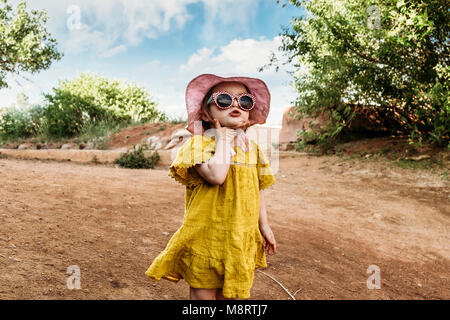 Ragazza carina indossando occhiali da sole e cappello mentre si sta in piedi sul campo Foto Stock