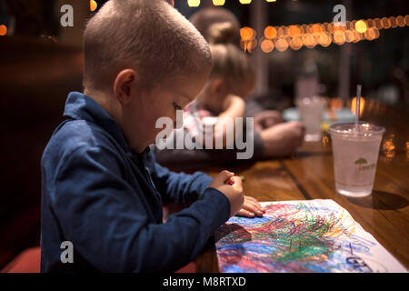Vista laterale del ragazzo la colorazione su carta al tavolo da pranzo in ristorante Foto Stock