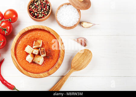 Zuppa Gazpacho con cracker, in un piatto di legno su un bianco sullo sfondo di legno. Nelle vicinanze si trovano i pomodori e spezie Foto Stock