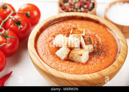 Zuppa Gazpacho con cracker, in un piatto di legno su un bianco sullo sfondo di legno. Nelle vicinanze si trovano i pomodori e spezie Foto Stock