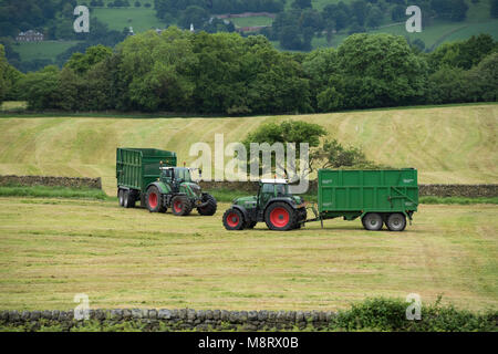 Lavorando in una fattoria campo, 2 green i trattori Fendt sono il traino di rimorchi - 1 viene caricato con erba tagliata per insilati & 1 è vuota - West Yorkshire, Inghilterra, Regno Unito Foto Stock