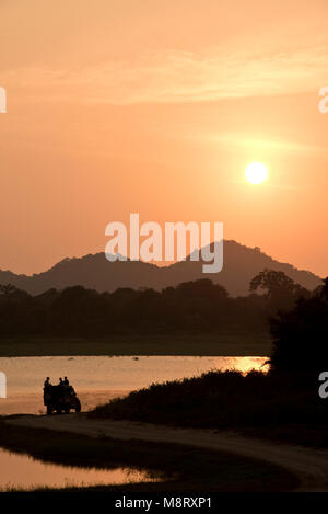 Minneriya National Park in Sri Lanka con un gruppo di turisti in una jeep 4 x 4 accanto a un lago guardando il caldo tramonto di sera. Foto Stock