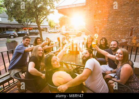 Ritratto di felice amici tostare birra seduti al cafè sul marciapiede durante la giornata di sole Foto Stock