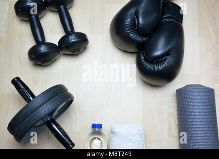 Kick Boxing guanti, a peso fisso barbells, ab ruota, bottiglia di acqua, asciugamano, materassino arrotolabile su sfondo di legno Foto Stock