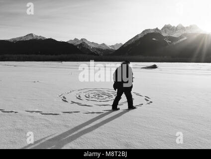 Uomo che fa un sprial nella neve come il sole tramonta sulla congelati Chilkat fiume vicino a Haines, Alaska. Foto Stock