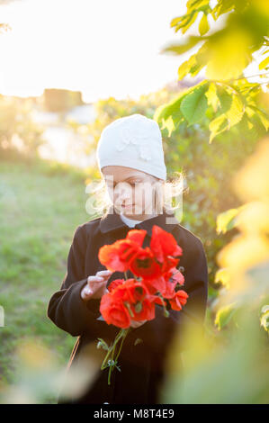 Bellissima bambina in hat e rivestire holding bouquet di fiori rossi in primavera Foto Stock