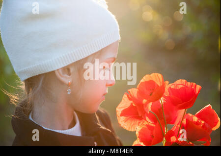 Trasognata bambina in bianco cappello di lana con profumo di arancio fiori di papavero retroilluminata con Tramonto primaverile Foto Stock