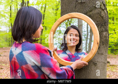 Giovane donna colombiano guardando lo specchio nella foresta di primavera Foto Stock