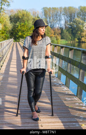 Giovane donna in piedi con le stampelle sul ponte di legno in natura Foto Stock