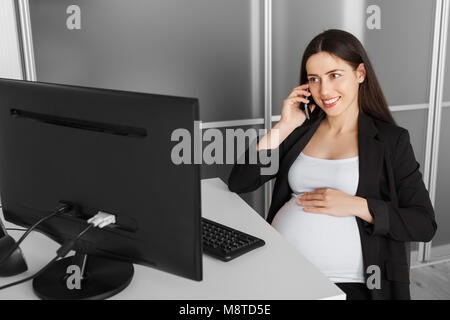 Donna incinta parlando al telefono in ufficio Foto Stock
