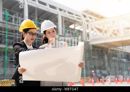 Due architetti femmina nella costruzione di caschi e occhiali di sicurezza guardando la costruzione dell'edificio blueprint. Un concetto architettonico discutendo con ciascun ot Foto Stock