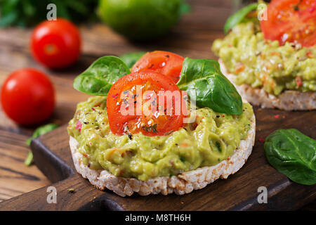 Una sana prima colazione. Sandwich di pane croccante con il guacamole e pomodori su un sfondo di legno. Foto Stock