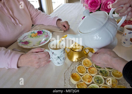 Due donne amici avente una tazza di tè del pomeriggio insieme. Senior donna versando una tazza di tè per un amico durante il tè del pomeriggio. Foto Stock