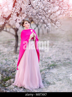 Giovane donna nei giardini del mandorlo in fiore in un bellissimo abito lungo Foto Stock