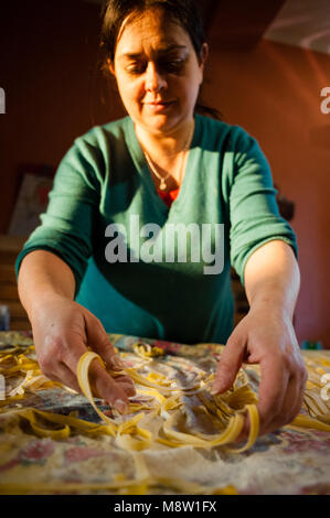 Il 40-anno-vecchia donna si prepara la pasta fresca all'uovo tagliatelle fatte in casa tesa sopra la tabella sotto la luce diretta del sole Foto Stock