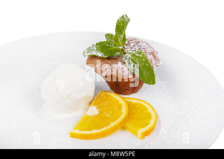 Tortina di cioccolato, muffin su una piastra bianca con fettine di arancia, menta e gelato alla vaniglia isolati su sfondo bianco. Dessert per un menu in un cafe, Foto Stock