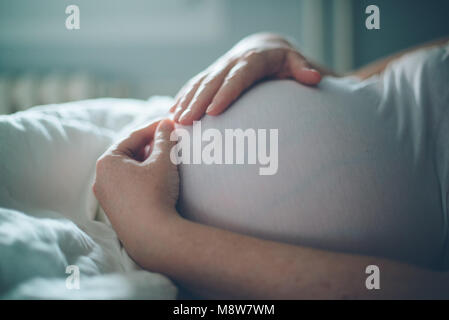 Donna incinta cuddling pancia in camera da letto a casa appena prima che il travaglio e il parto, il fuoco selettivo Foto Stock