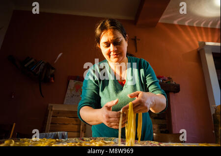 Il 40-anno-vecchia donna si prepara la pasta fresca all'uovo tagliatelle fatte in casa tesa sopra la tabella sotto la luce diretta del sole Foto Stock