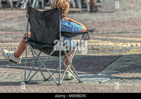 Il ragazzo è seduto in una sedia su un quadrato Foto Stock