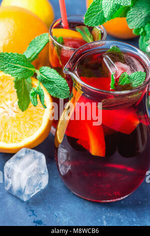 Analcoliche rinfrescante Sangria spagnola dalla varietà di frutti di agrumi arancio Melograno acini di uva e menta fresca nella brocca di vetro e sul blu B Foto Stock