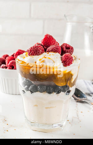 Una sana prima colazione, semola budino di porridge in vetro con il latte, la panna caramello e frutti di bosco, marmo bianco copia tabella spazio Foto Stock