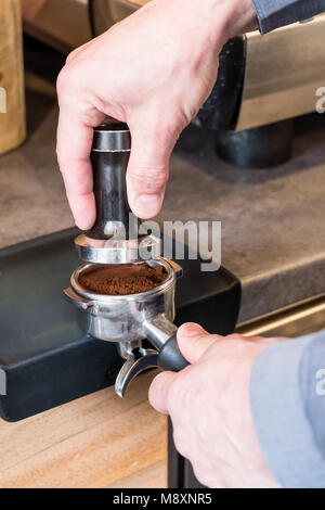 Barista immissione tamper oltre il caffè appena macinato in portafilter per fare caffè espresso o cappuccino Foto Stock