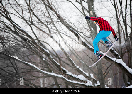 Immagine dell uomo sportive indossando il casco salti su snowboard sullo sfondo di inverno alberi Foto Stock