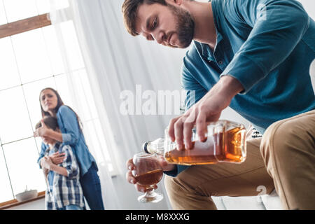 Madre padre e figlio problemi sociali alcolismo uomo di bere whisky close-up mentre la donna che copre gli occhi di capretto disperata di protezione Foto Stock