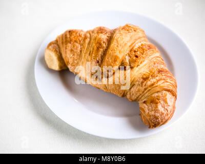 Vista orizzontale al di sopra di un unico croissant francesi su una piastra bianca e sfondo Foto Stock