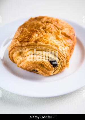 Vista verticale di un singolo francese croissant al cioccolato su una piastra bianca e sfondo Foto Stock