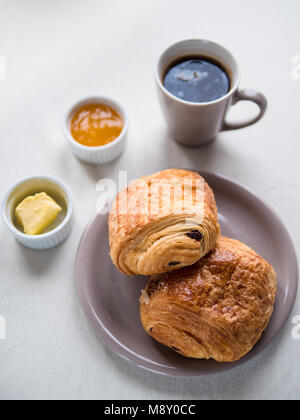 Vista al di sopra di una prima colazione continentale con il francese croissant al cioccolato, burro, marmellata e caffè nero su bianco nella tabella Foto Stock