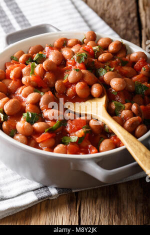 Stufati di mirtillo palustre o di fagioli borlotti in salsa di pomodoro con erbe di close-up in una ciotola sul piano verticale. Foto Stock