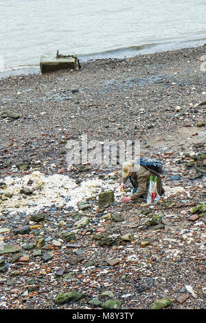 Un uomo In cerca e ricerca sull'foreshore del fiume Tamigi con la bassa marea. Foto Stock