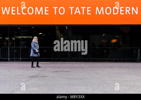 Una donna a piedi nella parte anteriore di un segno di benvenuto al di sopra di un ingresso alla Tate Gallery di Londra. Foto Stock