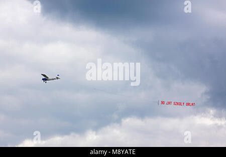 Aeroplano Yakovlev Yak-12M (Jak-12; "Creek') banner di traino oltre il cielo nuvoloso durante il novantesimo anniversario del polacco Air Force Academy " Scuola di Eaglets'. Foto Stock