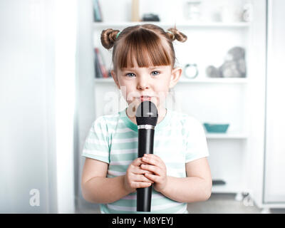 Carino bambina cantando il karaoke a casa. Foto Stock