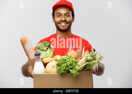 Concetto di consegna - Bello americano africano uomo consegna portando scatola di imballaggio del negozio di generi alimentari il cibo e le bevande dal negozio. Isolato su grigio di sfondo per studio. Copia dello spazio. Foto Stock