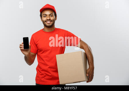 Concetto di consegna - Ritratto di bello americano africano uomo di consegna o corriere con box che mostra il telefono cellulare su di lei per controllare l'ordine. Isolato su grigio di sfondo per studio. Copia dello spazio. Foto Stock