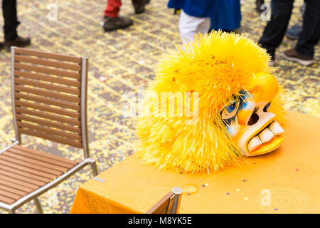 Il Carnevale di Basilea 2018. Gerbergasse, Basilea, Svizzera - Febbraio 19th, 2018. Close-up di un singolo giallo maschera di Carnevale posa su un ristorante tabella Foto Stock