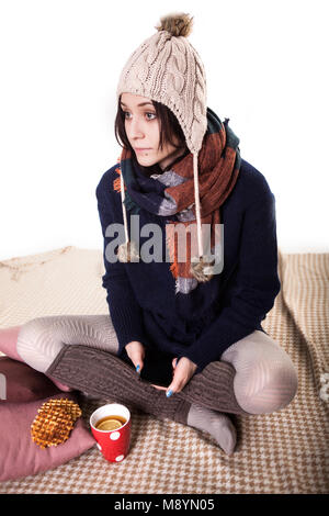 Sorridenti Hipster ragazza in maglione e Beanie Hat con una tazza in mani. Bella Donna a muro bianco sullo sfondo. In inverno o in autunno in fase di riscaldamento. Foto Stock