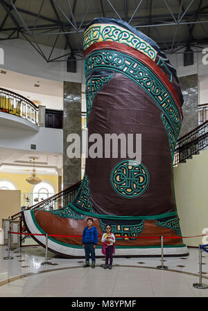 I bambini in piedi accanto alla più grande del mondo di scarpe, un gigante tradizionale mongola in avvio di Chinggis Khaan statua complessa, Tsonjin Boldog, Mongolia Foto Stock