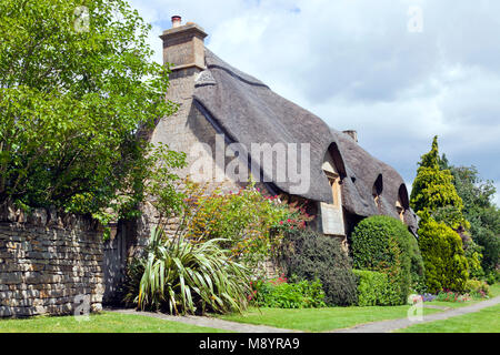 Villaggio percorso lungo il suggestivo tetto di paglia casa inglese nelle zone rurali del Cotswold campagna, con fiori, arbusti, alberi giardino anteriore, , su un soleggiato d estate Foto Stock