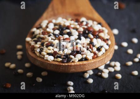 Materie miste di quinoa (Chenopodium quinoa). Rosso, bianco e nero semi in cucchiaio di legno su sfondo nero Foto Stock