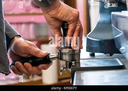 Barista premendo caffè appena macinato con dispositivo antimanomissione in portafilter per fare caffè espresso o cappuccino Foto Stock
