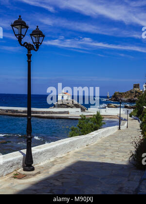 Piccoli semafori sulla strada nei pressi del porto, con una piccola cappella e il faro bianco in background Foto Stock