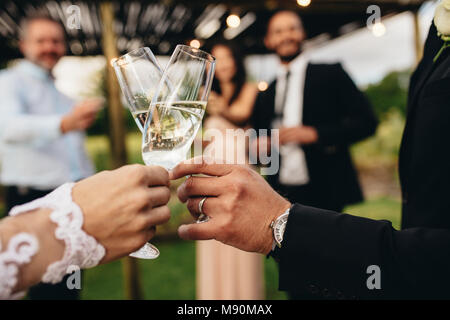Chiudere di nuovo coppia sposata tostatura bicchieri di champagne al party di nozze. Sposa e lo sposo mani tintinnanti bicchieri al ricevimento di nozze. Foto Stock