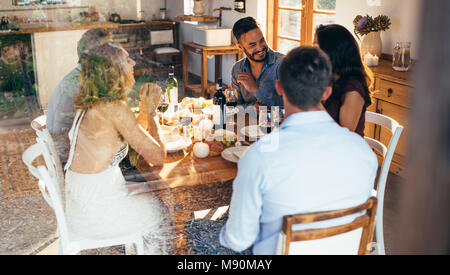 Giovani amici ad un tavolo a parlare nel corso del pranzo a casa. gruppo di uomini e donne godendo di pasto a casa insieme. Foto Stock